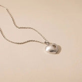 Silver heart-shaped pendant necklace on a beige background